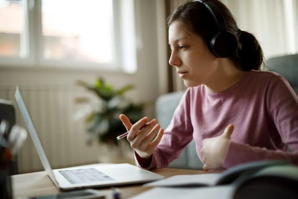 High school girl in pink shirt speaks into her laptop. Here are some tips on how to contact a college after applying.