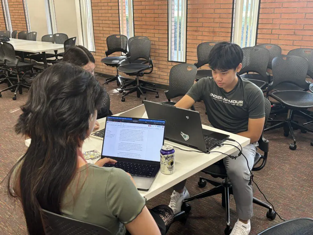 Two students in a USC Summer Programs course study at their laptops in a classroom with brick walls. Here's how to succeed as a first-generation college student.