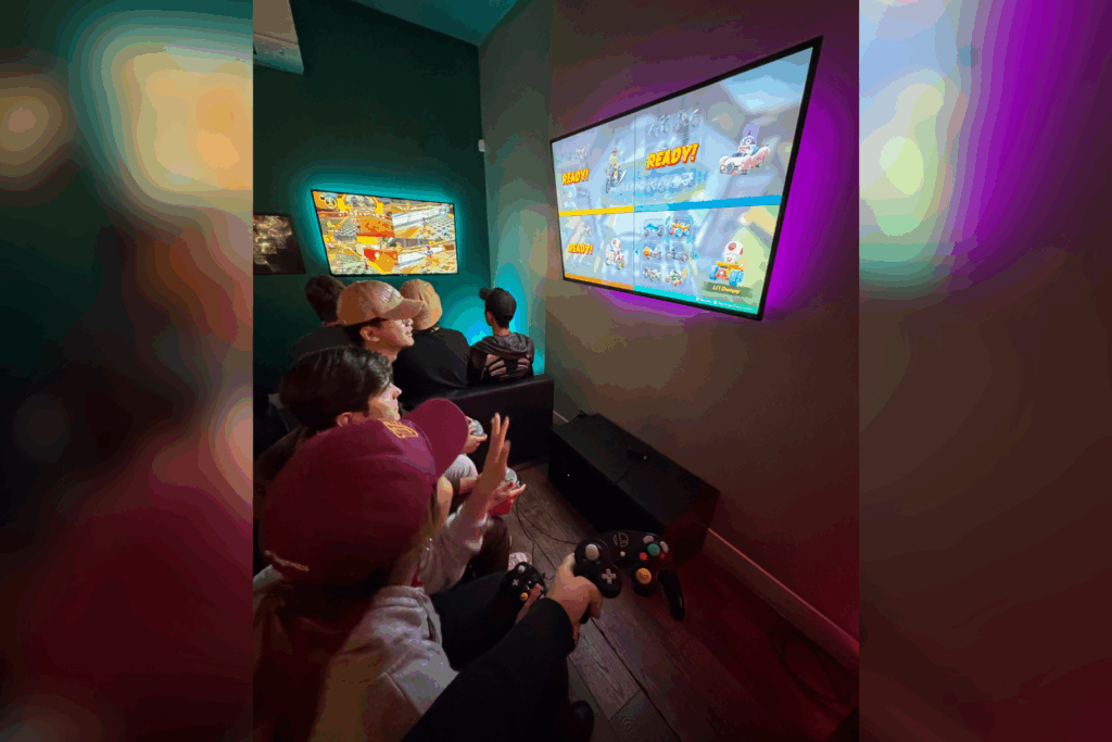 USC Summer Programs students sit in front of flat screen TV playing video game at Neon Retro Arade