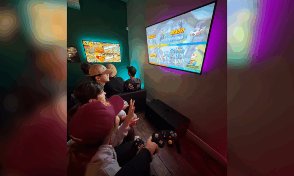 USC Summer Programs students sit in front of flat screen TV playing video game at Neon Retro Arade