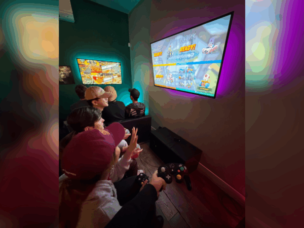 USC Summer Programs students sit in front of flat screen TV playing video game at Neon Retro Arade