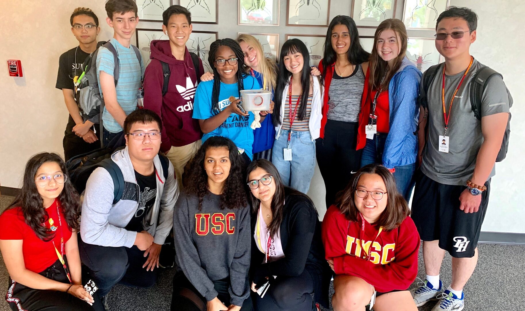 A group of students pose together indoors, smiling and wearing USC apparel and ID lanyards.