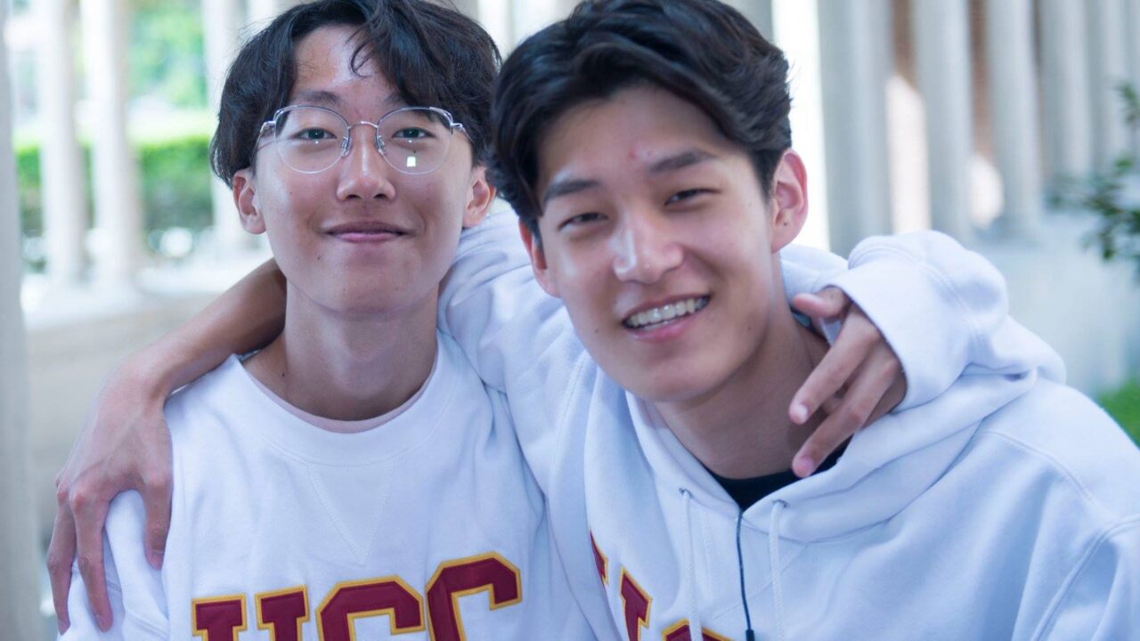 Two students wearing USC hoodies smiling with arms around each other.