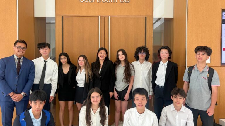 A group of students and an instructor stand outside a courtroom labeled “Courtroom 8B,” dressed formally and smiling for a photo.