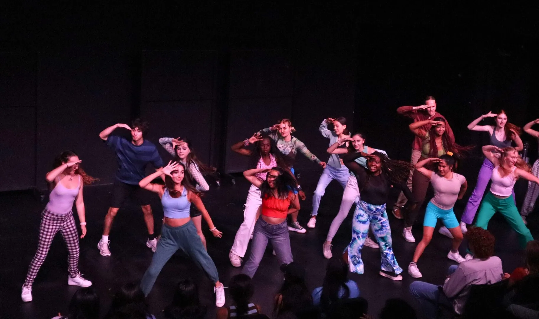 Musical theatre students dance on stage in a dark theatre.