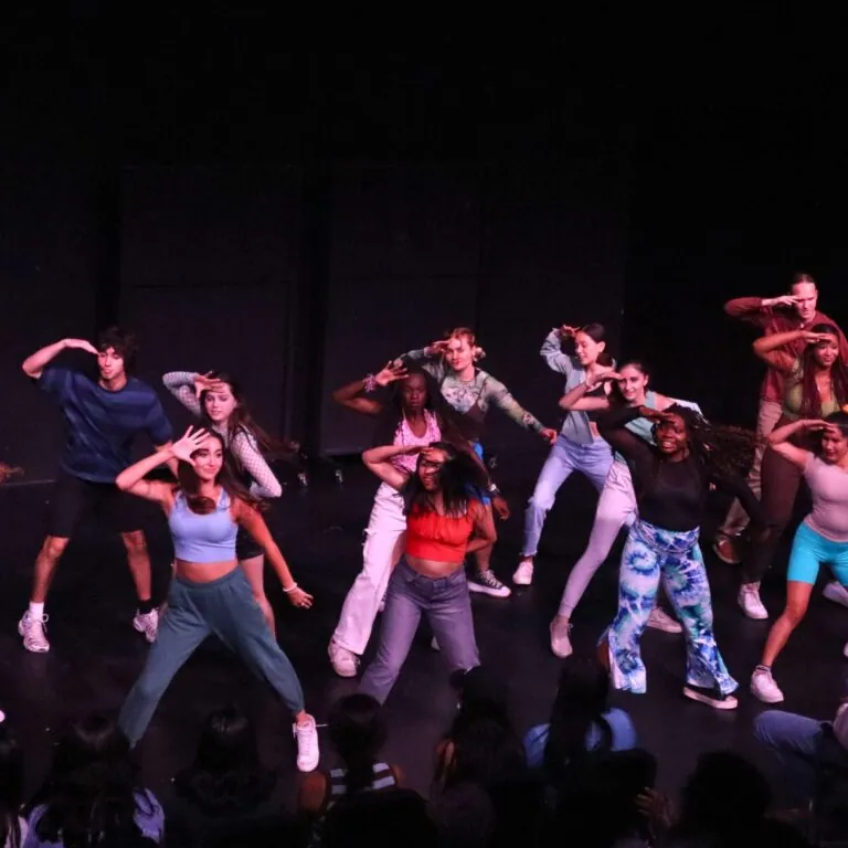 Musical theatre students dance on stage in a dark theatre.
