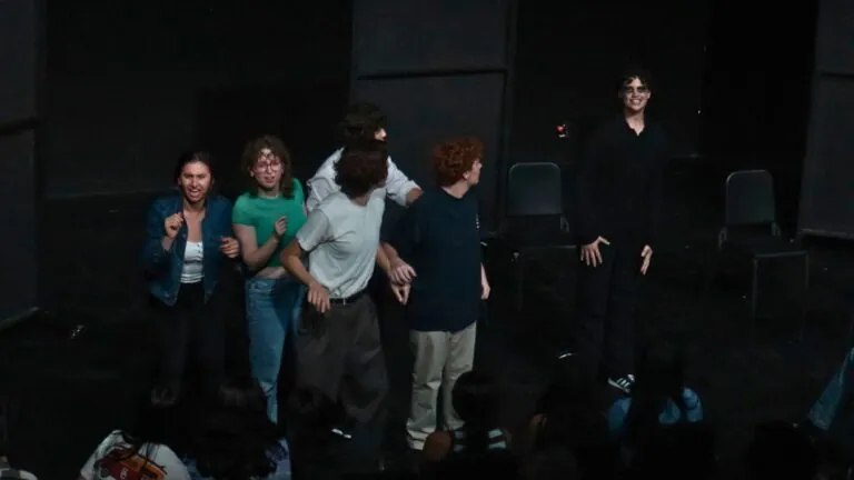 Musical theatre students act on stage in a dark theatre.