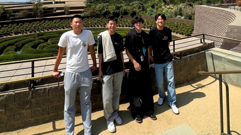 Four boys pose outdoors against a railing at The Getty on a stone balcony.