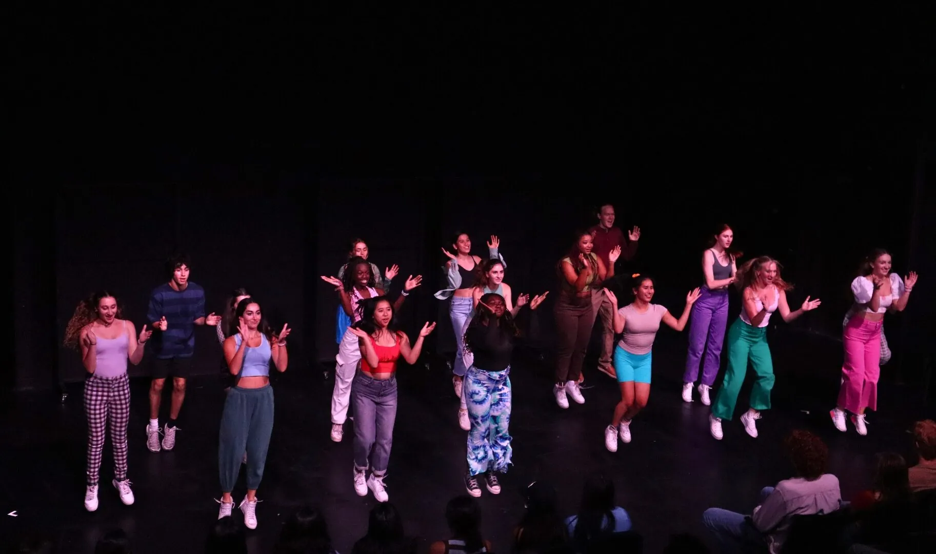 Students in the musical theatre summer program dance on a dark stage.
