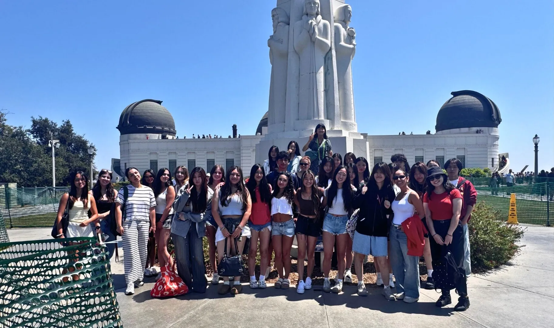 A group of students stands together in front of the Griffith Observatory monument in Los Angeles on a sunny day, posing for a group photo during a field trip.