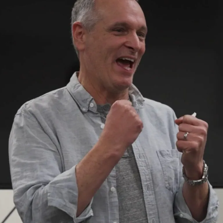 An instructor gestures while speaking during an online lesson, emphasizing a point to virtual students.