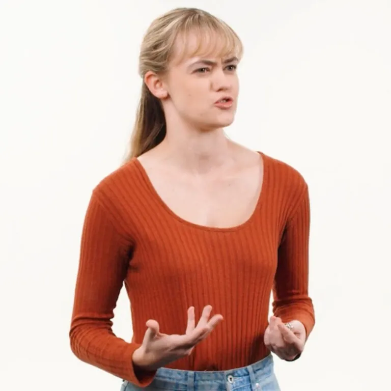 A young woman in a rust-colored sweater speaks expressively during an online class discussion against a white background.