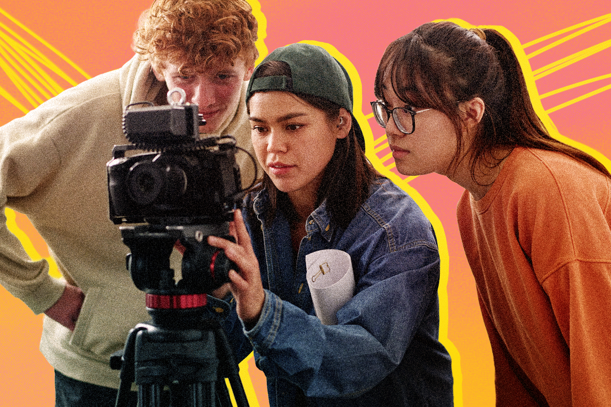 [Graphic] Three young adults gather around a professional video camera mounted on a tripod, with the person in the center wearing a backward baseball cap and denim shirt while adjusting the camera. A pink and orange gradient background features bright yellow outlines around the group and diagonal decorative lines.