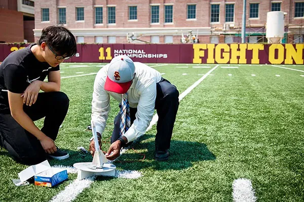 USC faculty member and high school student preparing a small rocket model on a campus athletic field, representing hands-on learning and exploration in USC Pre-College Summer Programs.