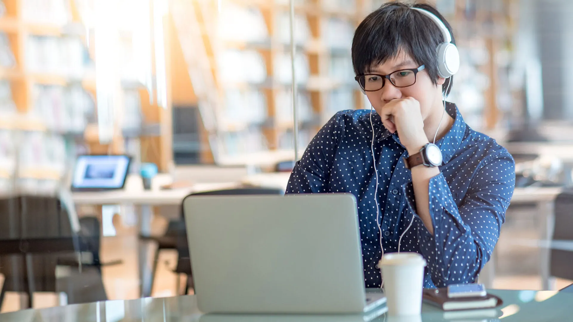 Focused student wearing headphones studying on a laptop in a library, representing USC Pre-College online course “Building Blocks of Business: Tools for Creating a Dynamic and Sustainable Business,” where learners study at their own pace and earn a Certificate of Completion.