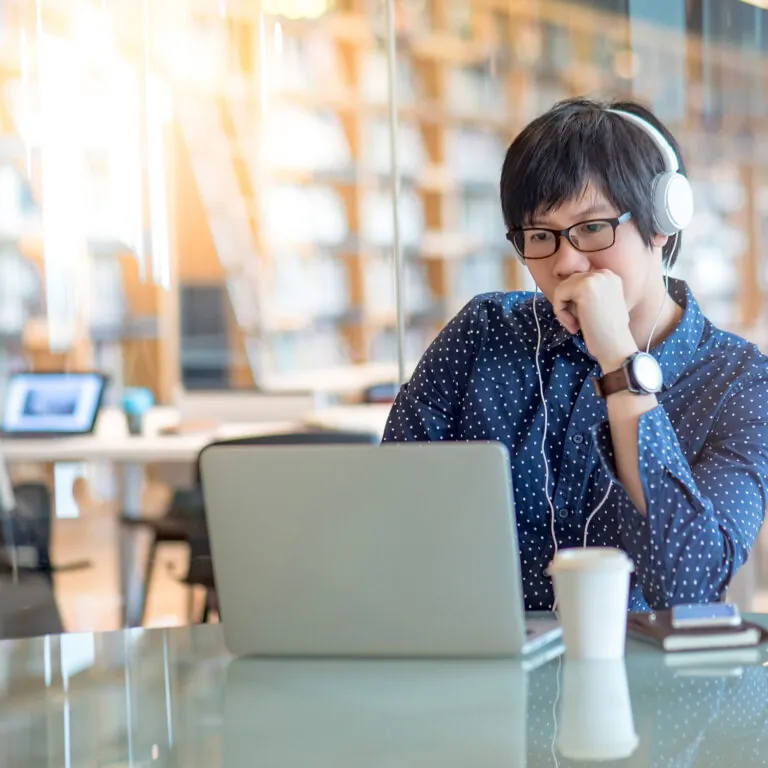 Focused student wearing headphones studying on a laptop in a library, representing USC Pre-College online course “Building Blocks of Business: Tools for Creating a Dynamic and Sustainable Business,” where learners study at their own pace and earn a Certificate of Completion.
