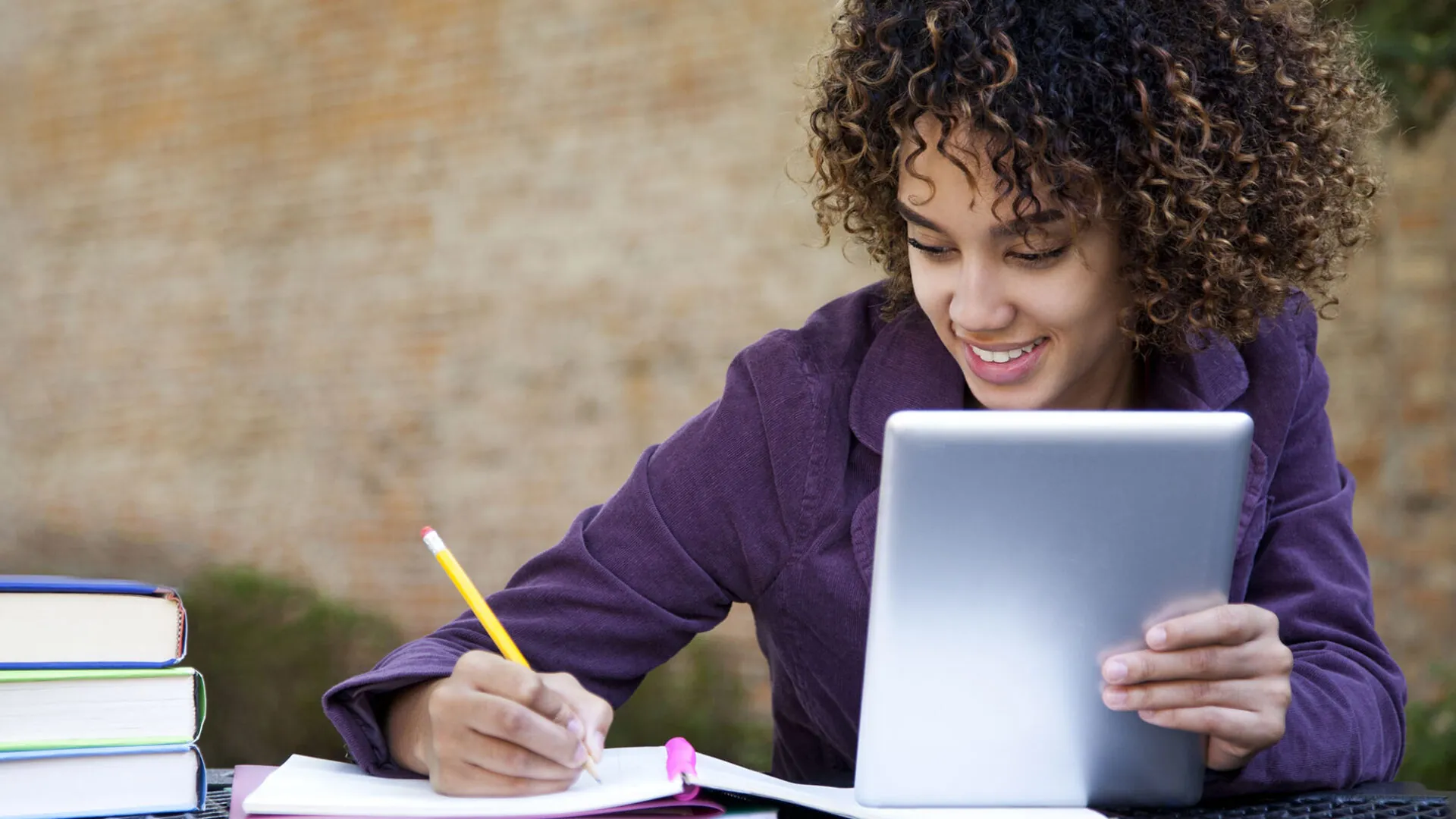 Smiling student studying outdoors with a tablet and notebook, representing USC Pre-College online course “Introduction to Cybersecurity: From Securing Systems to Ethical Hacking,” where students learn flexibly and earn a Certificate of Completion.