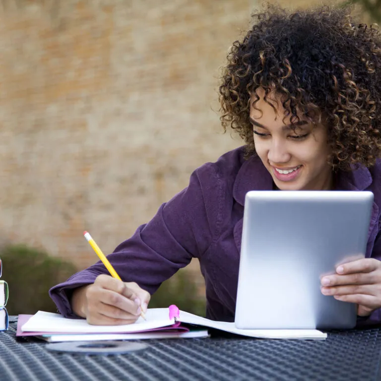 Smiling student studying outdoors with a tablet and notebook, representing USC Pre-College online course “Introduction to Cybersecurity: From Securing Systems to Ethical Hacking,” where students learn flexibly and earn a Certificate of Completion.