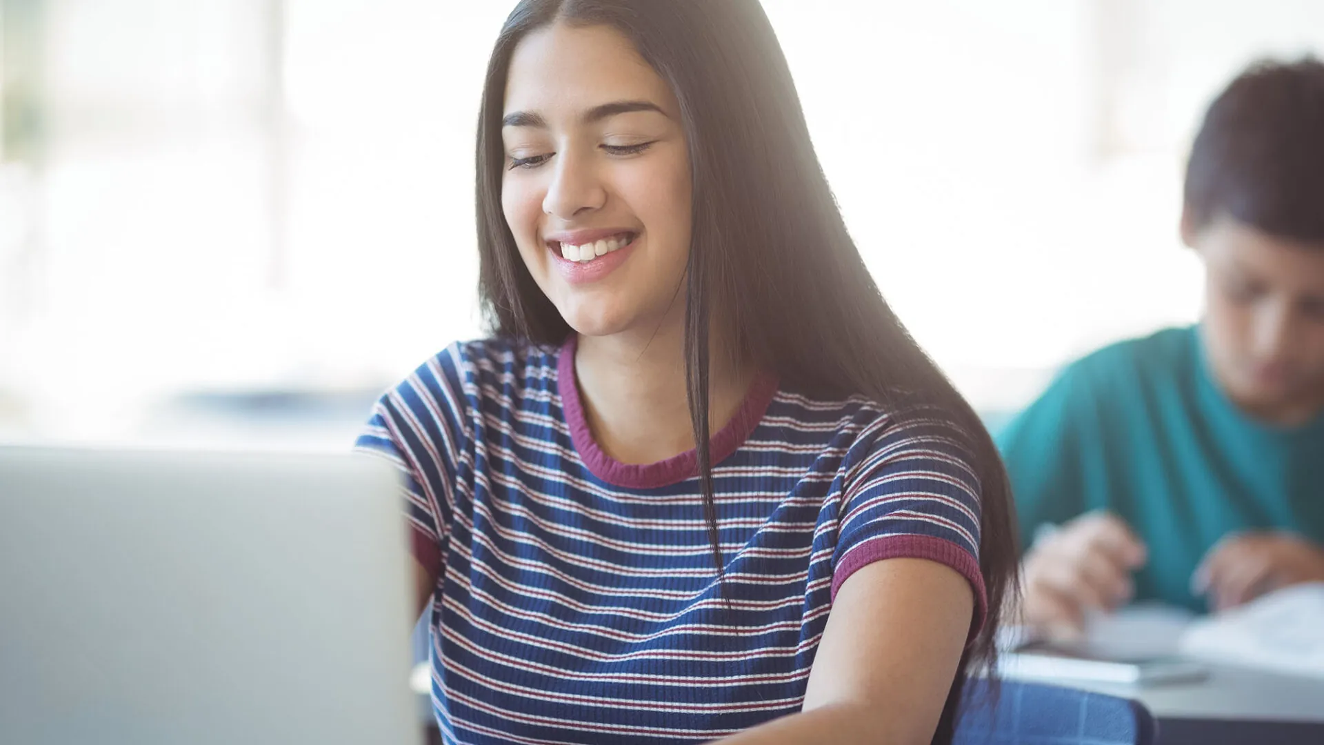 Smiling student working on a laptop in a classroom, representing USC Pre-College online course “Entrepreneurship: Exploring What It Takes to Create Your Own Business,” where students learn at their own pace and earn a Certificate of Completion.