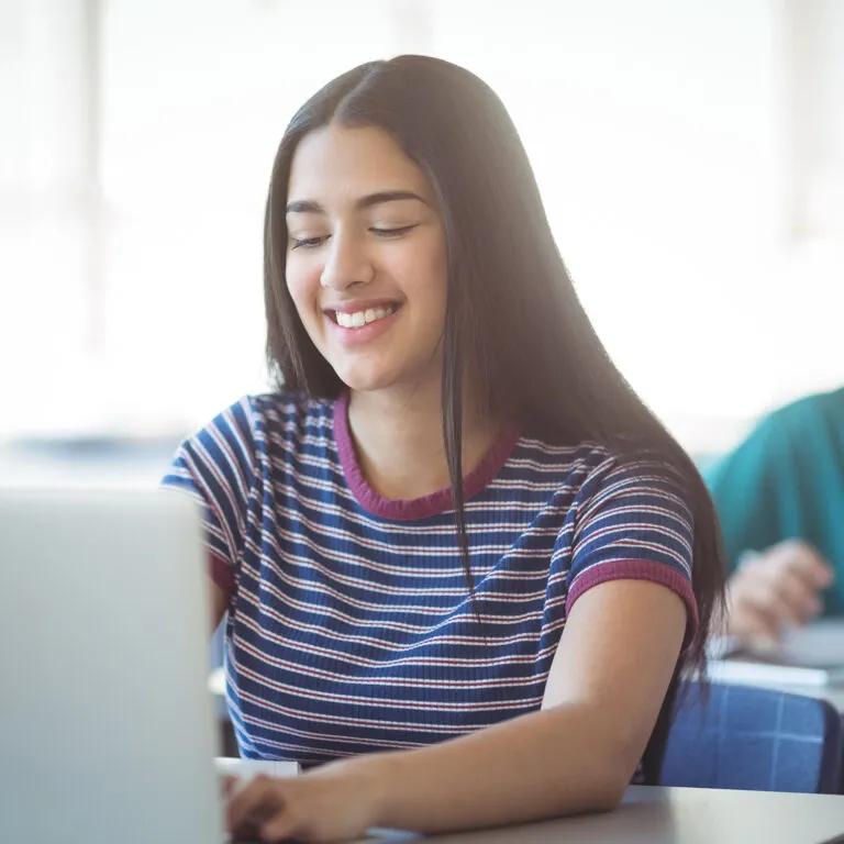 Smiling student working on a laptop in a classroom, representing USC Pre-College online course “Entrepreneurship: Exploring What It Takes to Create Your Own Business,” where students learn at their own pace and earn a Certificate of Completion.