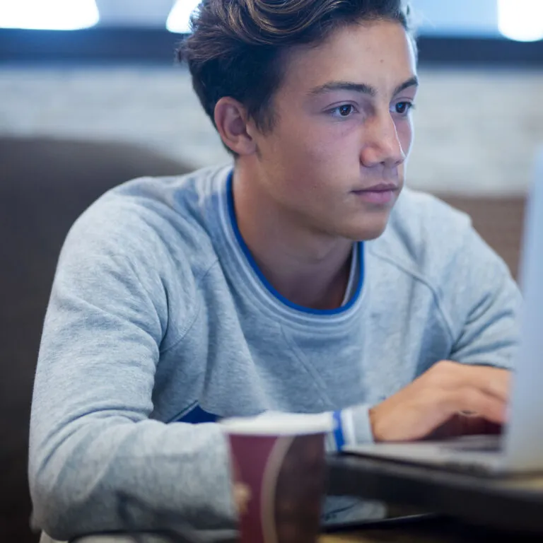 Focused student working on a laptop with a coffee cup nearby, representing USC Pre-College online course “Finance: From Personal Literacy to Global Markets,” where learners study at their own pace and earn a Certificate of Completion.