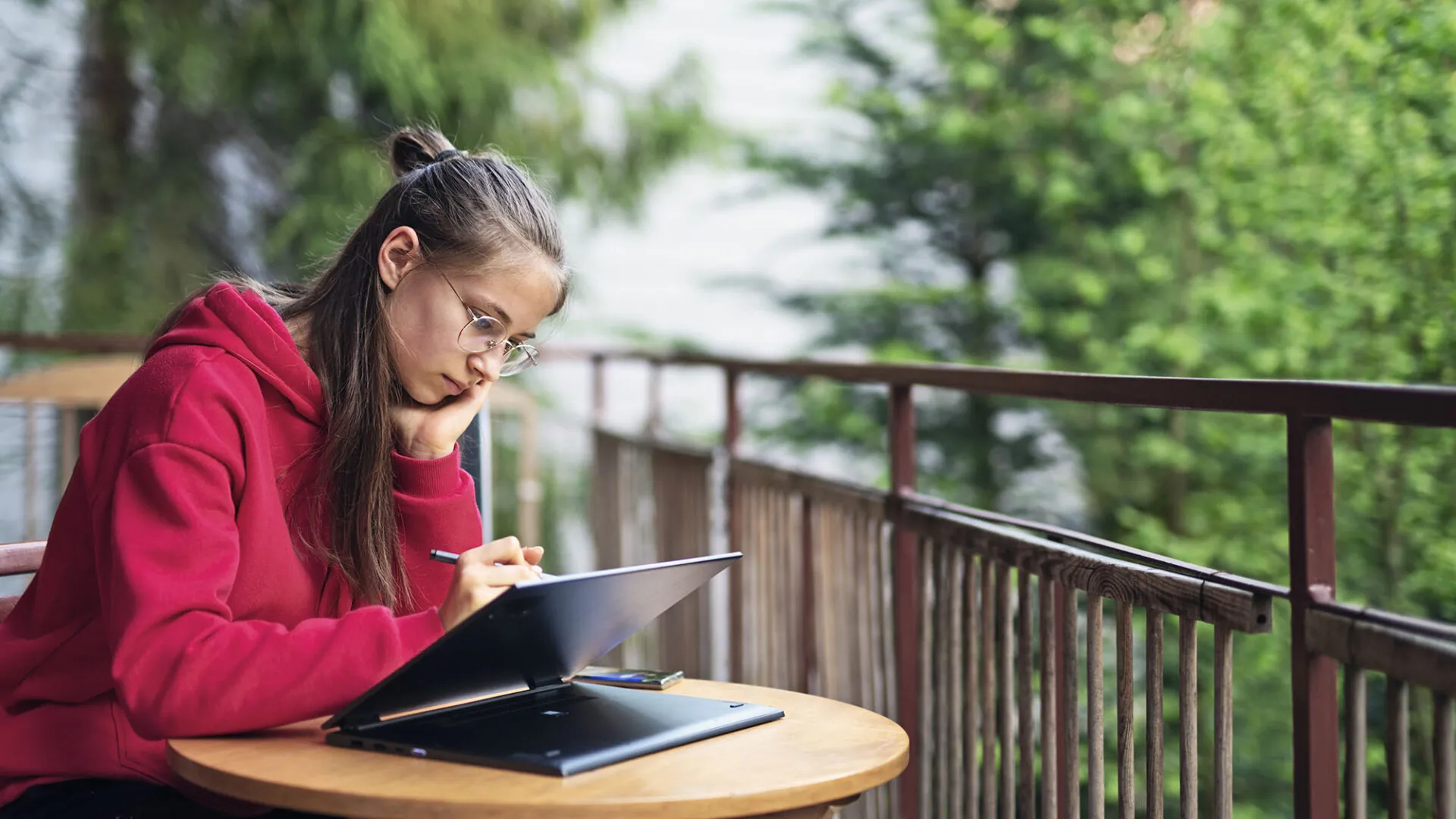 Focused student in a red hoodie studying on a tablet at an outdoor table, representing USC Pre-College online course “Lifespan Development: Critical Questions for Aging and the Lifespan,” where students learn independently and earn a Certificate of Completion.