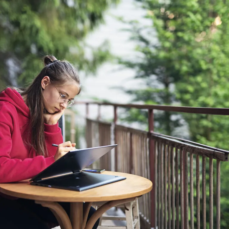 Focused student in a red hoodie studying on a tablet at an outdoor table, representing USC Pre-College online course “Lifespan Development: Critical Questions for Aging and the Lifespan,” where students learn independently and earn a Certificate of Completion.