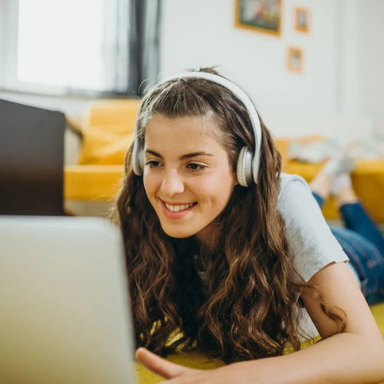 Smiling student wearing headphones and studying on a laptop at home, representing USC Pre-College online course “Digital Marketing: From Content Creation to Strategic Planning,” where students learn flexibly and earn a Certificate of Completion.