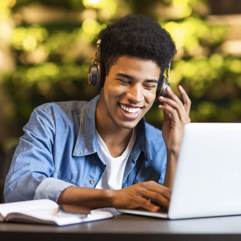 Smiling student wearing headphones and working on a laptop in a bright study space, representing USC Pre-College online course “Media and Social Change: Becoming a Change Agent for a Better World,” where students learn at their own pace and earn a Certificate of Completion.