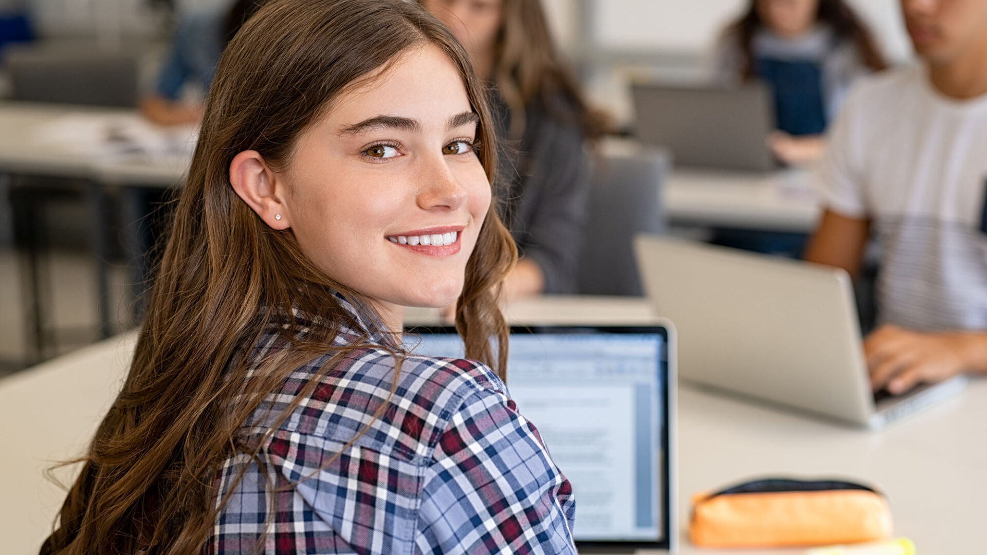 Smiling student sitting in a classroom and working on a laptop, representing USC Pre-College online course “Political Science: Impact, Activism and Your Career,” where students learn flexibly and earn a Certificate of Completion.