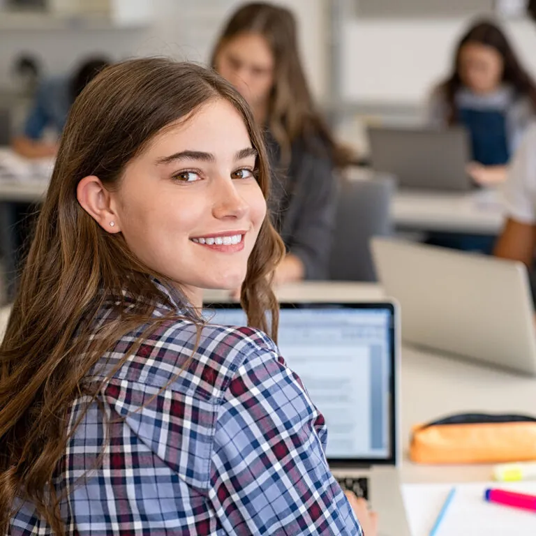 Smiling student sitting in a classroom and working on a laptop, representing USC Pre-College online course “Political Science: Impact, Activism and Your Career,” where students learn flexibly and earn a Certificate of Completion.