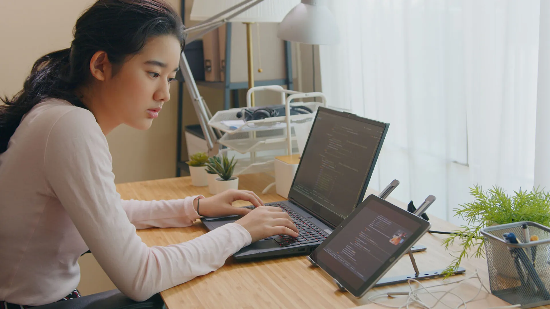 Focused high school student coding on a laptop and tablet at a study desk, representing USC Pre-College online courses that let students explore academic interests with flexibility.