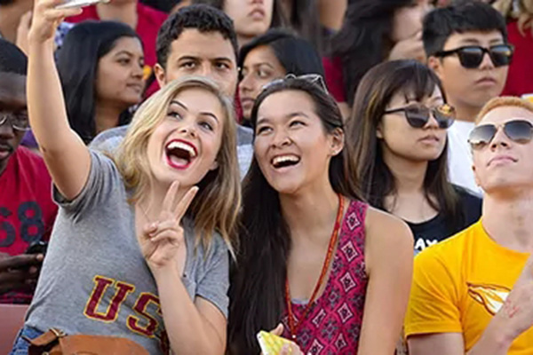 Excited USC students taking a selfie in the stands during a campus event, representing the vibrant student community featured in USC Undergraduate Admission.